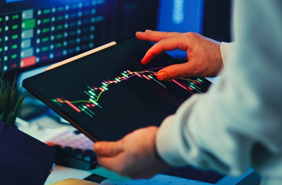 Five FTMO Alternatives Worth Switching To in 2026 3 A close-up of a person using a tablet to analyze stock market trends and charts indoors.